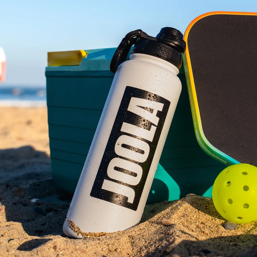 Bình JOOLA 40oz bản trắng đặt cạnh vợt và bóng pickleball trên sân